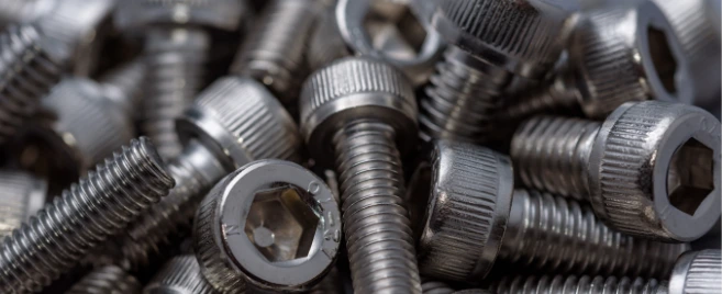 A close-up of a pile of shiny, silver-colored socket cap screws.