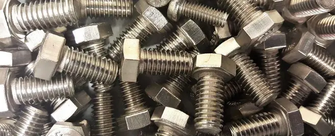 A close-up of a pile of shiny, silver-colored hexagonal head bolts.